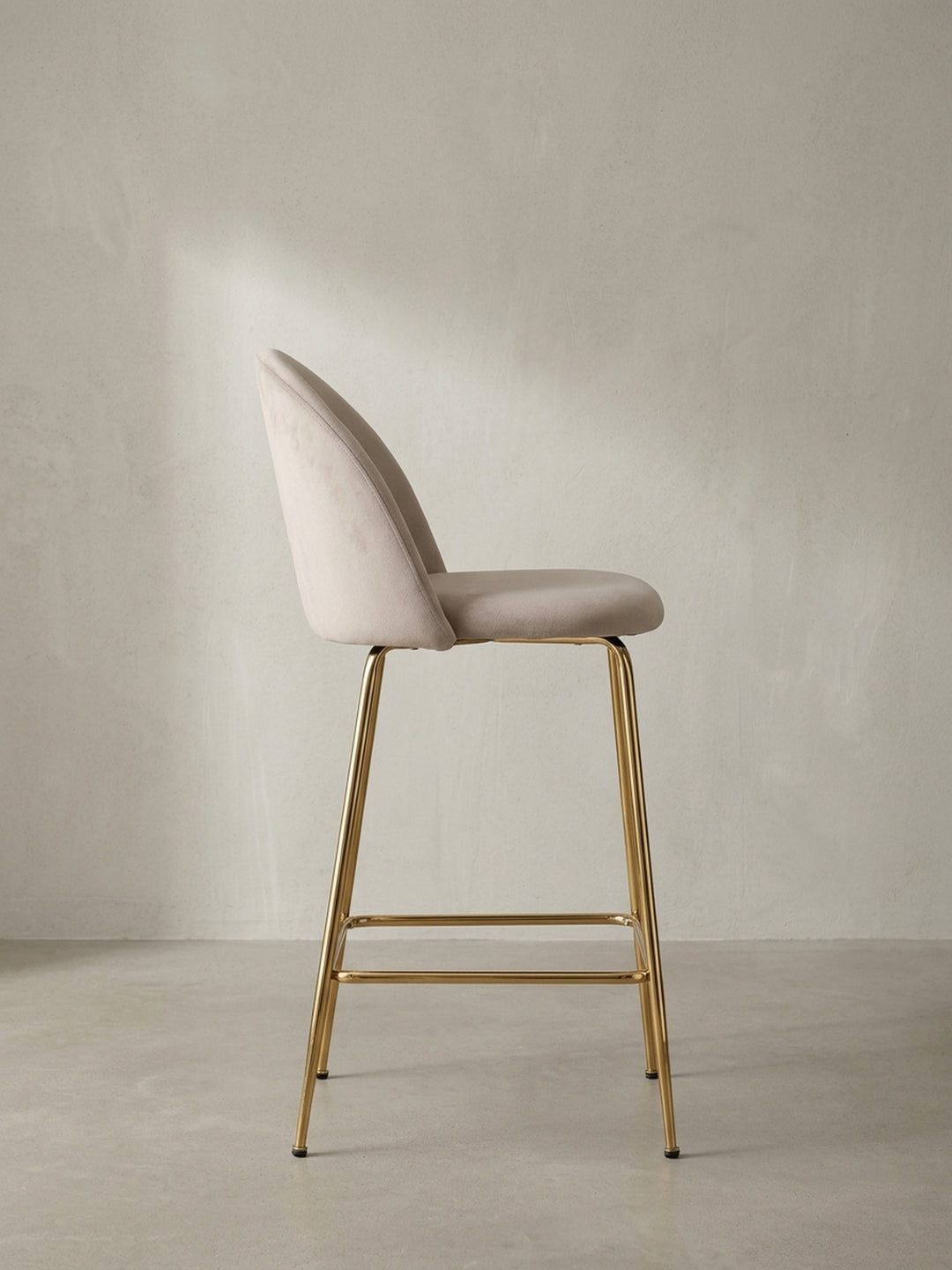 Design-Barstuhl mit Stoffbezug in Samt-Beige und einem filigranen Gestell aus goldfarbenem Metall als Gesamtansicht._