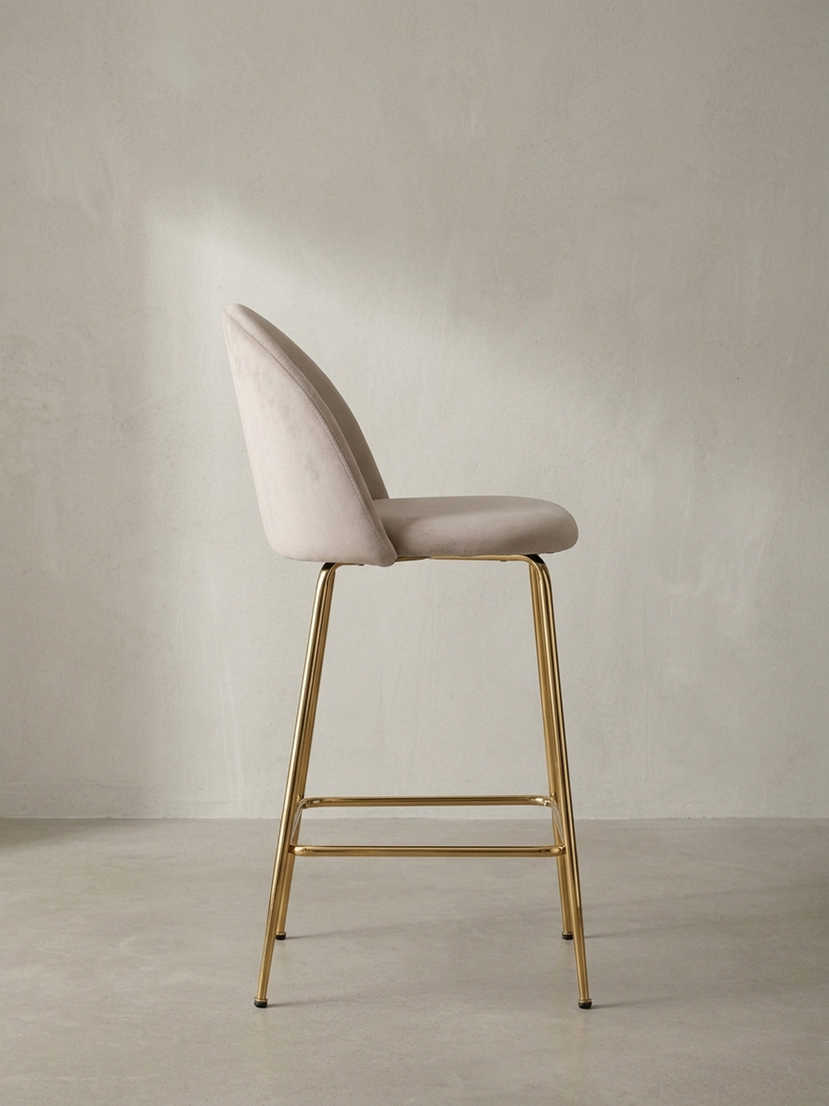 Design-Barstuhl mit Stoffbezug in Samt-Beige und einem filigranen Gestell aus goldfarbenem Metall als Gesamtansicht._
