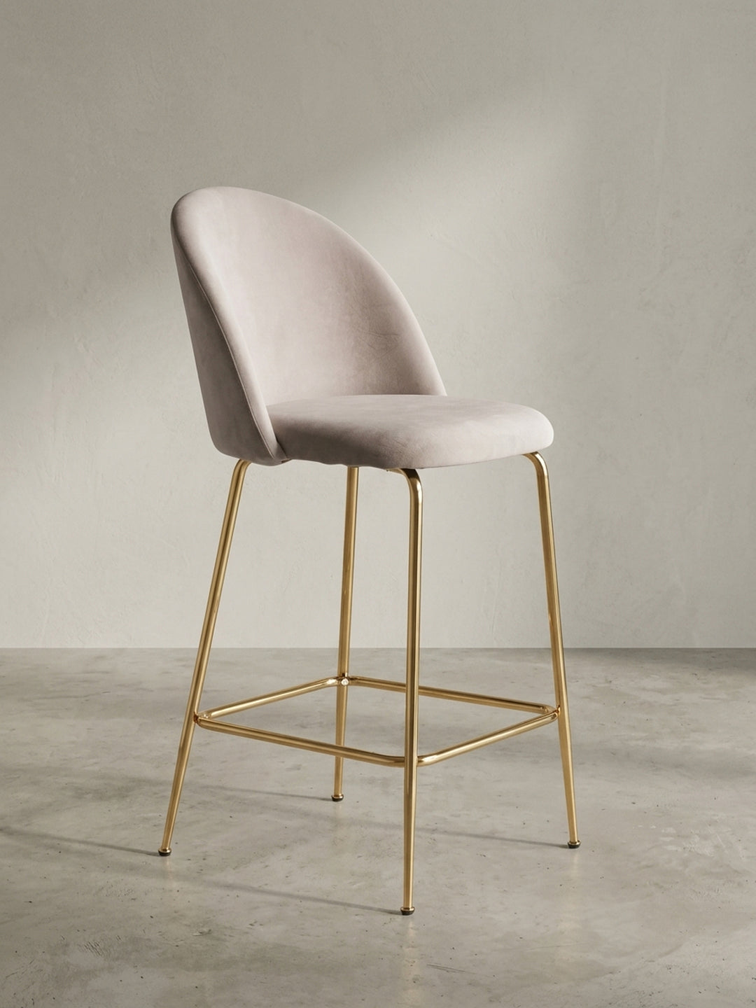 Der skandinavische Barhocker in Beige und Gold in einer Dreiviertelansicht, die die geschwungene Rückenlehne und Sitzfläche zeigt._