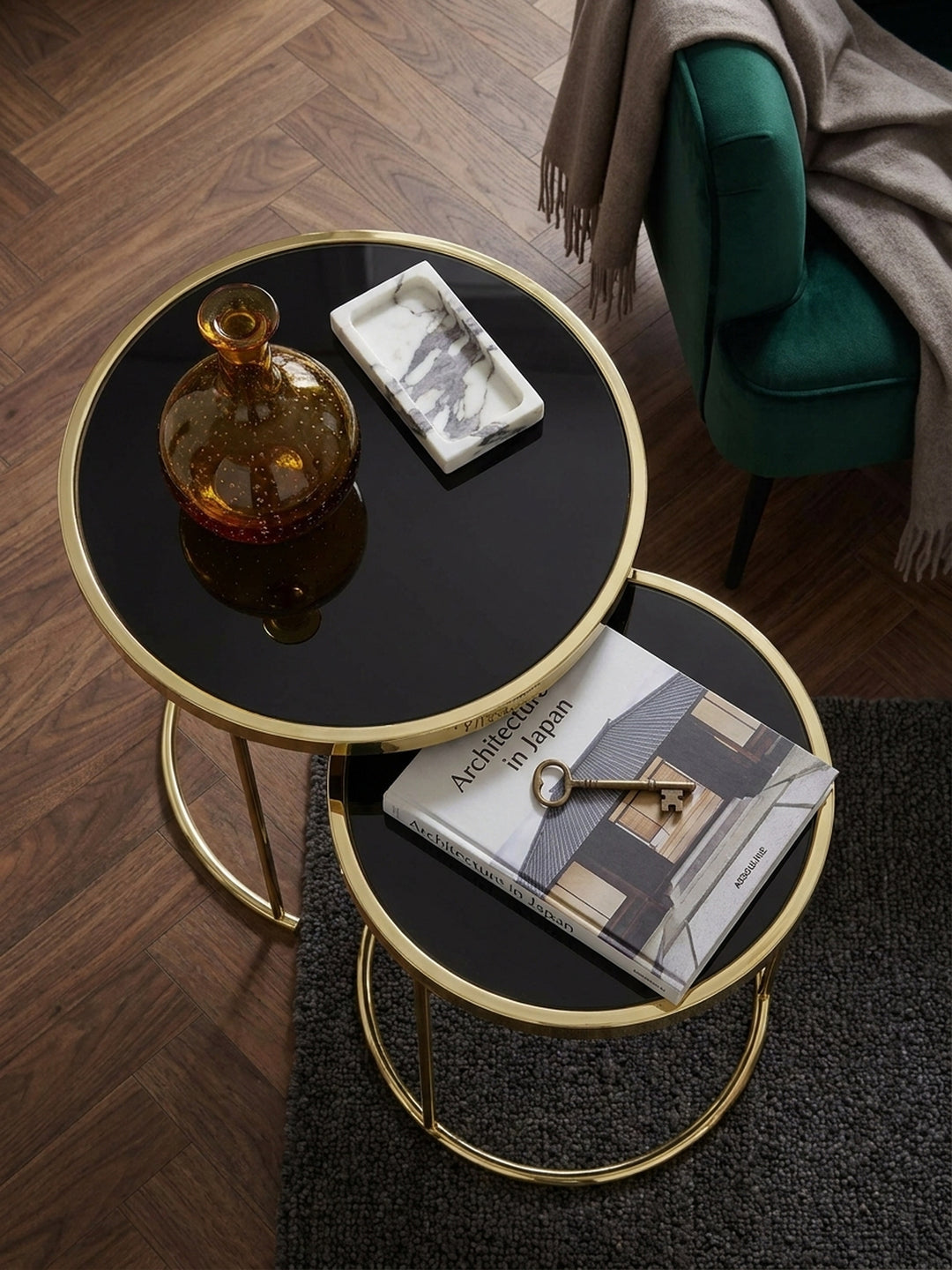 Draufsicht auf das platzsparende Couchtisch Set aus Metall und Glas neben einem smaragdgrünen Samtsessel auf dunklem Nussholzparkett_