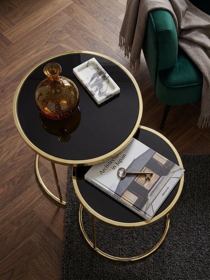 Draufsicht auf das platzsparende Couchtisch Set aus Metall und Glas neben einem smaragdgrünen Samtsessel auf dunklem Nussholzparkett_