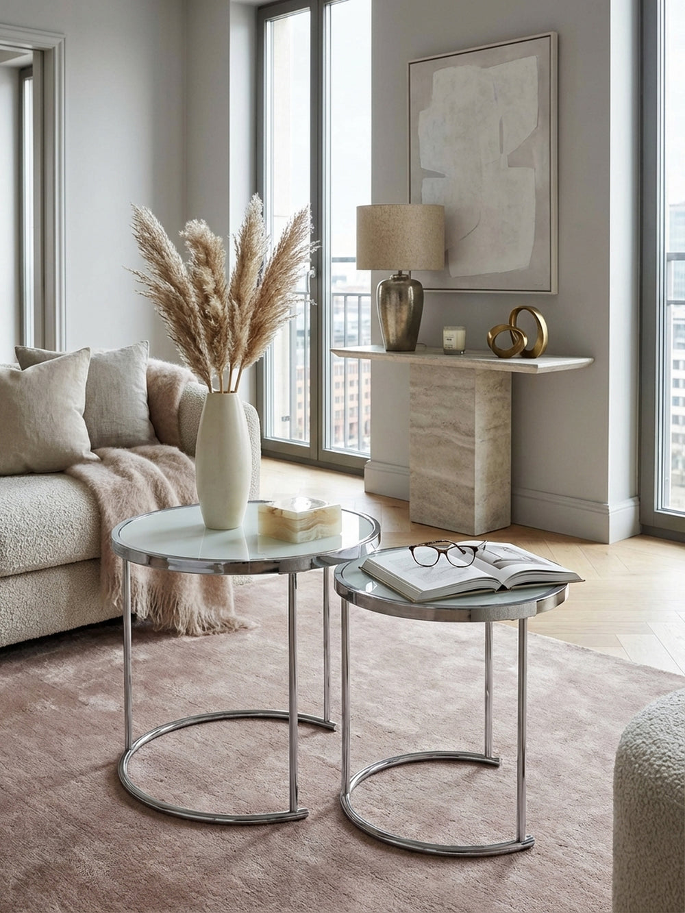 Moderner Satztisch in Silber und Weiß im stilvollen Wohnzimmer neben einem Sessel, dekoriert mit Glasvasen auf einem strukturierten Teppich für ein elegantes Ambiente._