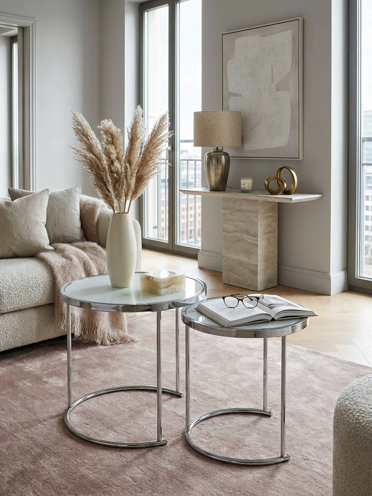 Moderner Satztisch in Silber und Weiß im stilvollen Wohnzimmer neben einem Sessel, dekoriert mit Glasvasen auf einem strukturierten Teppich für ein elegantes Ambiente._