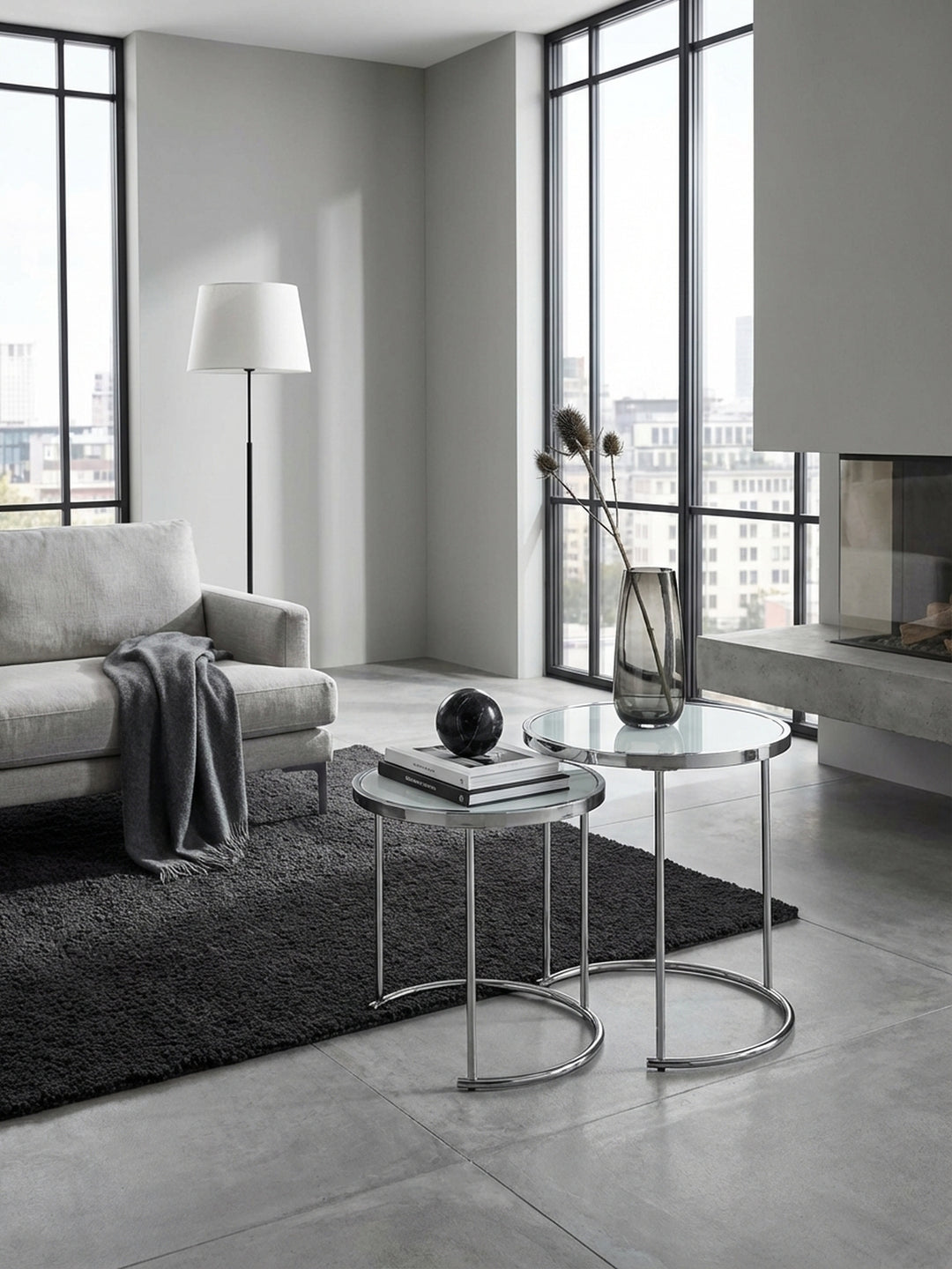 Moderner Satztisch in Silber und Weiß im stilvollen Wohnzimmer neben einem Sessel, dekoriert mit Glasvasen auf einem strukturierten Teppich für ein elegantes Ambiente._