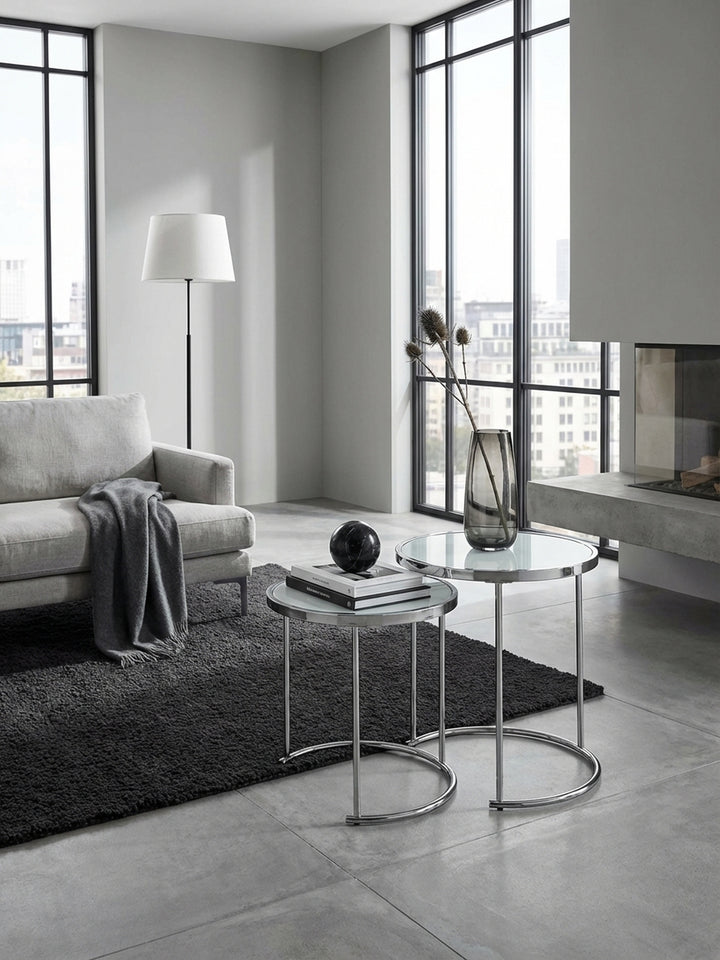 Moderner Satztisch in Silber und Weiß im stilvollen Wohnzimmer neben einem Sessel, dekoriert mit Glasvasen auf einem strukturierten Teppich für ein elegantes Ambiente._