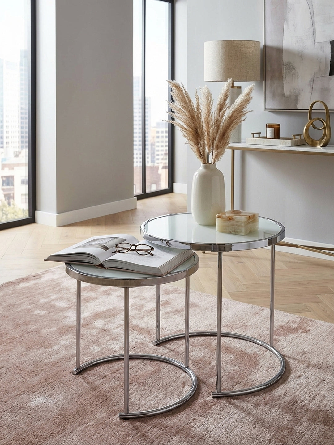 Design Beistelltisch 2er Set von oben, zeigt die runde Glasplatte in Weiß und das verchromte Metallgestell auf einem cremefarbenen Teppich mit schwarzen Akzenten._