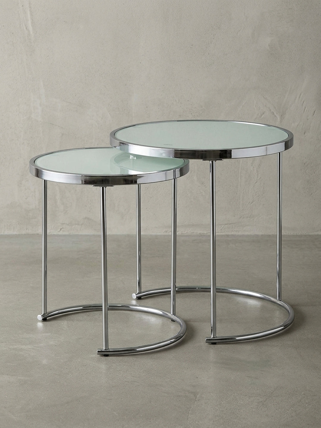 Runder Design Satztisch mit Gestell aus Chrom und weißer Glasplatte auf weißem Hintergrund, Frontalansicht des 2er Sets ineinander geschoben, Maße 50 und 42 cm Durchmesser._