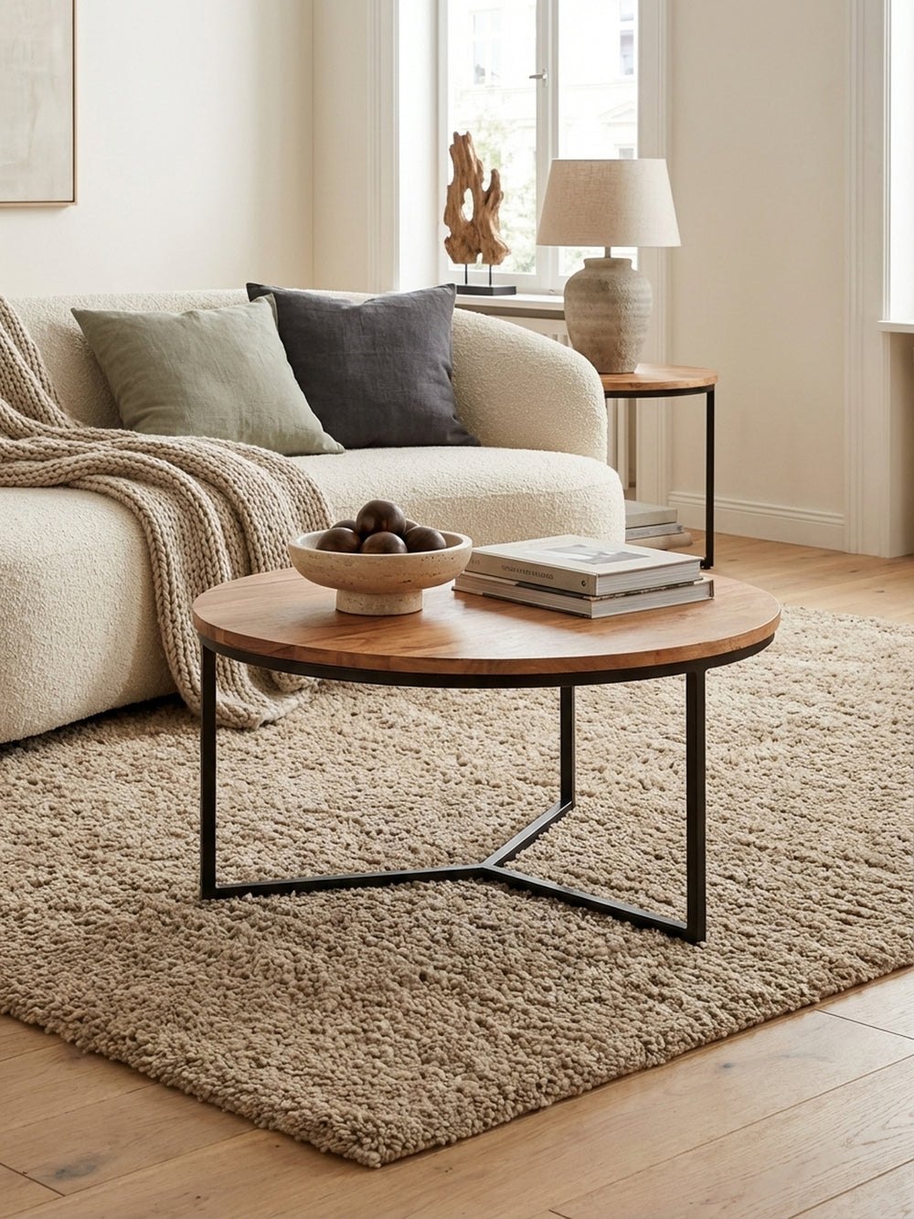 Eleganter runder Couchtisch aus Akazie Massivholz mit schwarzem Metallgestell in einem hellen, modernen Wohnzimmer, perfekt neben einem Sofa platziert._