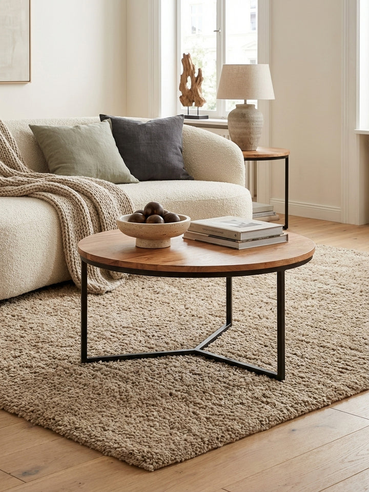 Eleganter runder Couchtisch aus Akazie Massivholz mit schwarzem Metallgestell in einem hellen, modernen Wohnzimmer, perfekt neben einem Sofa platziert._