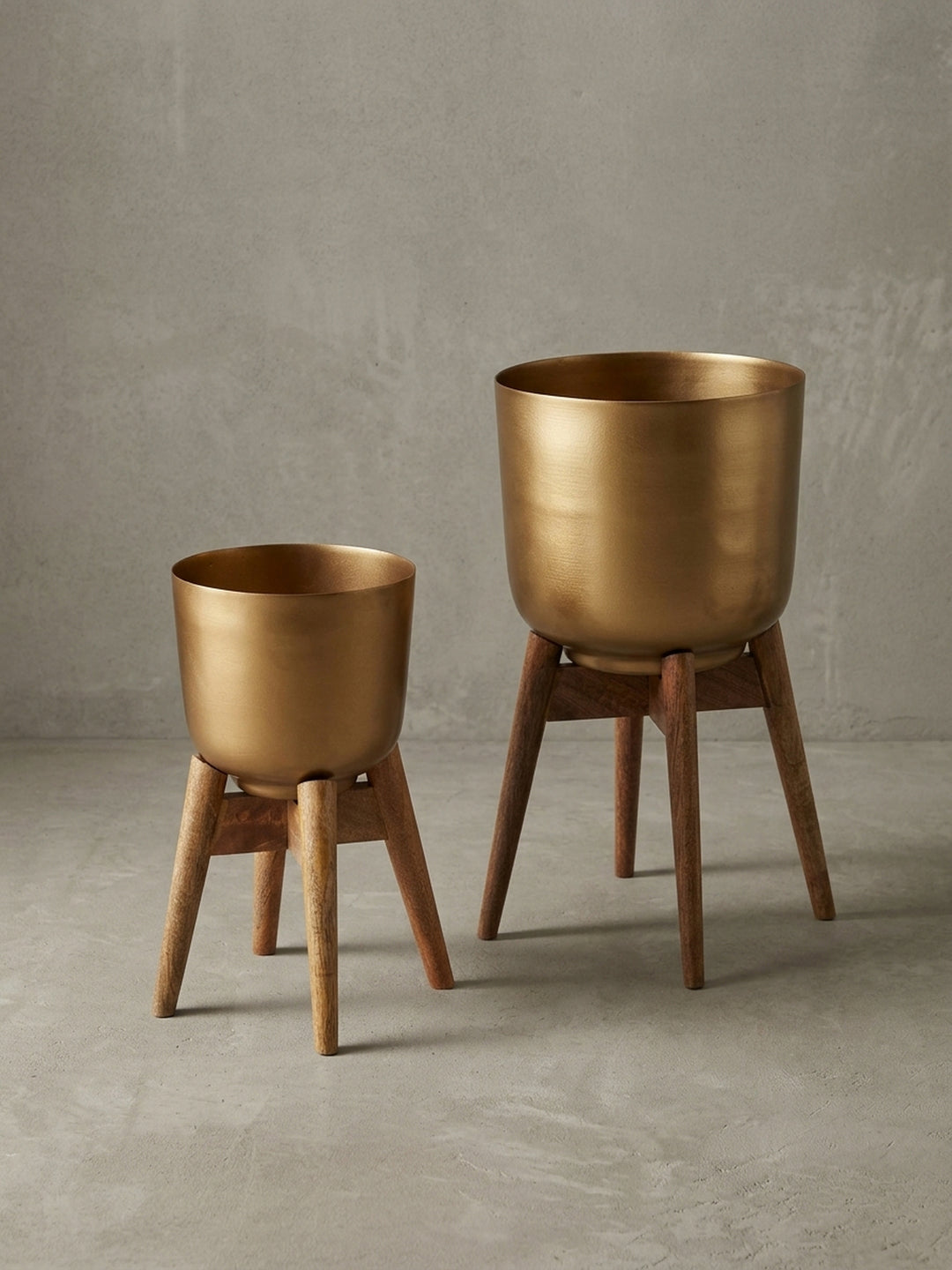 Seitenansicht des goldenen Blumenkübels mit Holzfüßen, das minimalistische Profil und die stabile Dreibein-Konstruktion betonend._