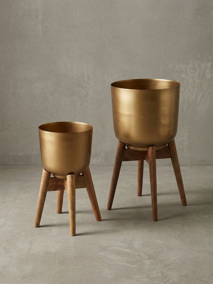 Seitenansicht des goldenen Blumenkübels mit Holzfüßen, das minimalistische Profil und die stabile Dreibein-Konstruktion betonend._