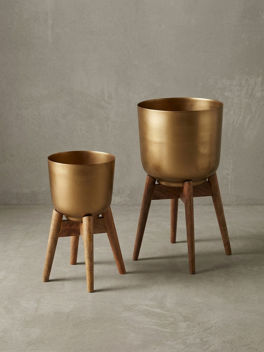 Seitenansicht des goldenen Blumenkübels mit Holzfüßen, das minimalistische Profil und die stabile Dreibein-Konstruktion betonend._