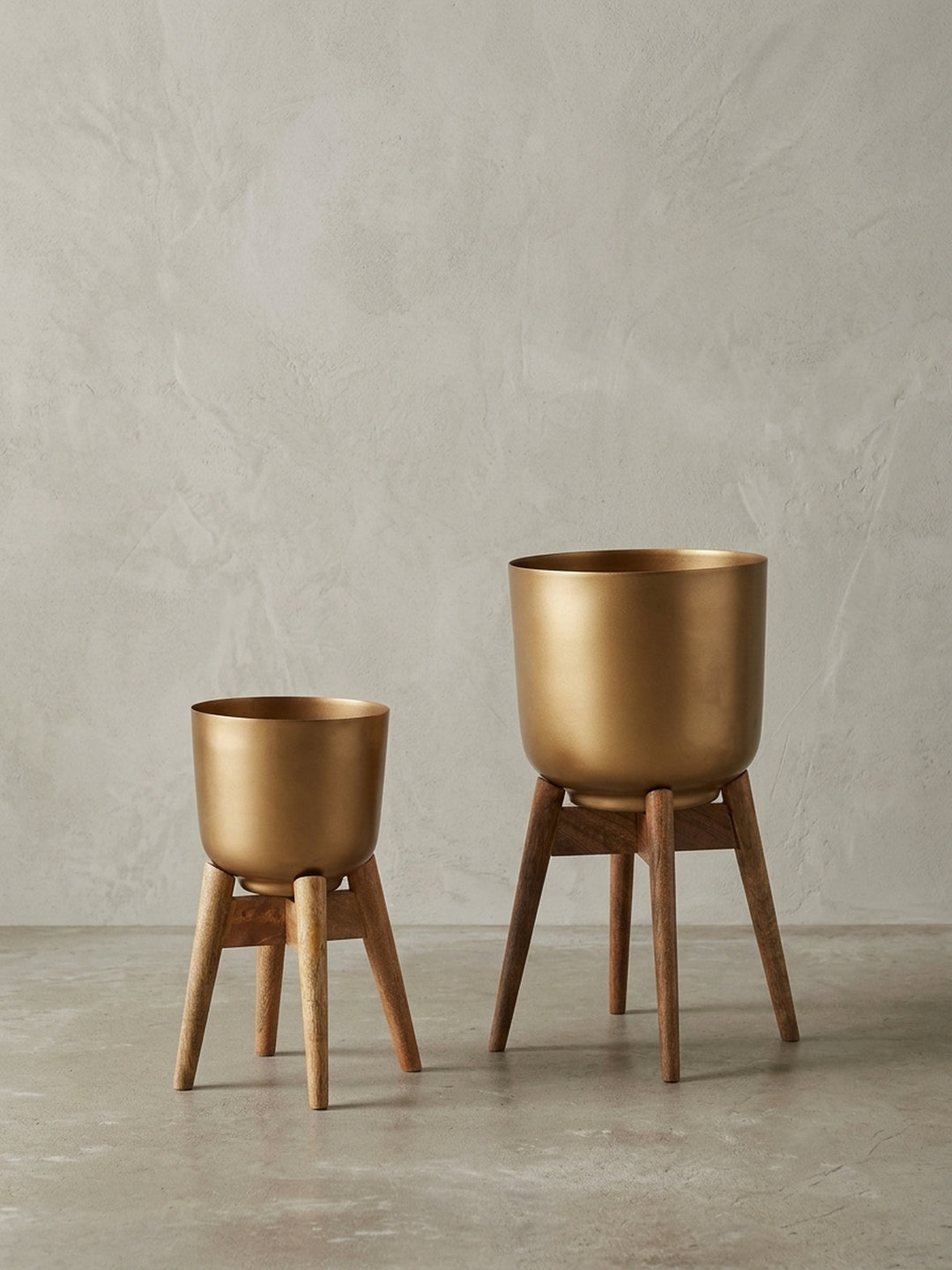 Zweiteiliges Set aus goldenen Pflanzgefäßen auf Mangoholz-Gestell, frontale Studioaufnahme vor weißem Hintergrund._