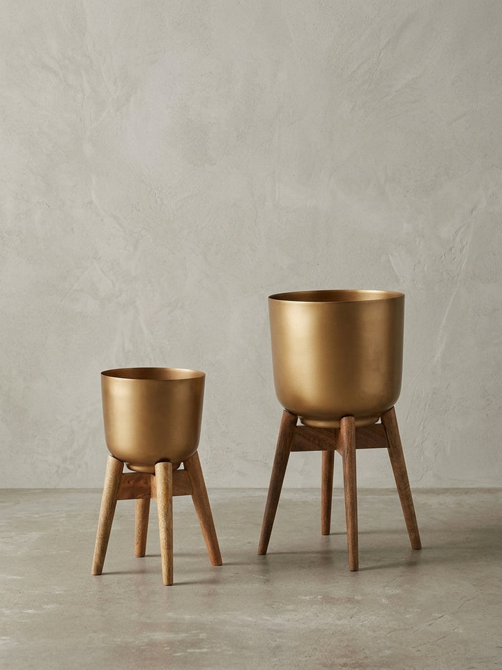 Zweiteiliges Set aus goldenen Pflanzgefäßen auf Mangoholz-Gestell, frontale Studioaufnahme vor weißem Hintergrund._