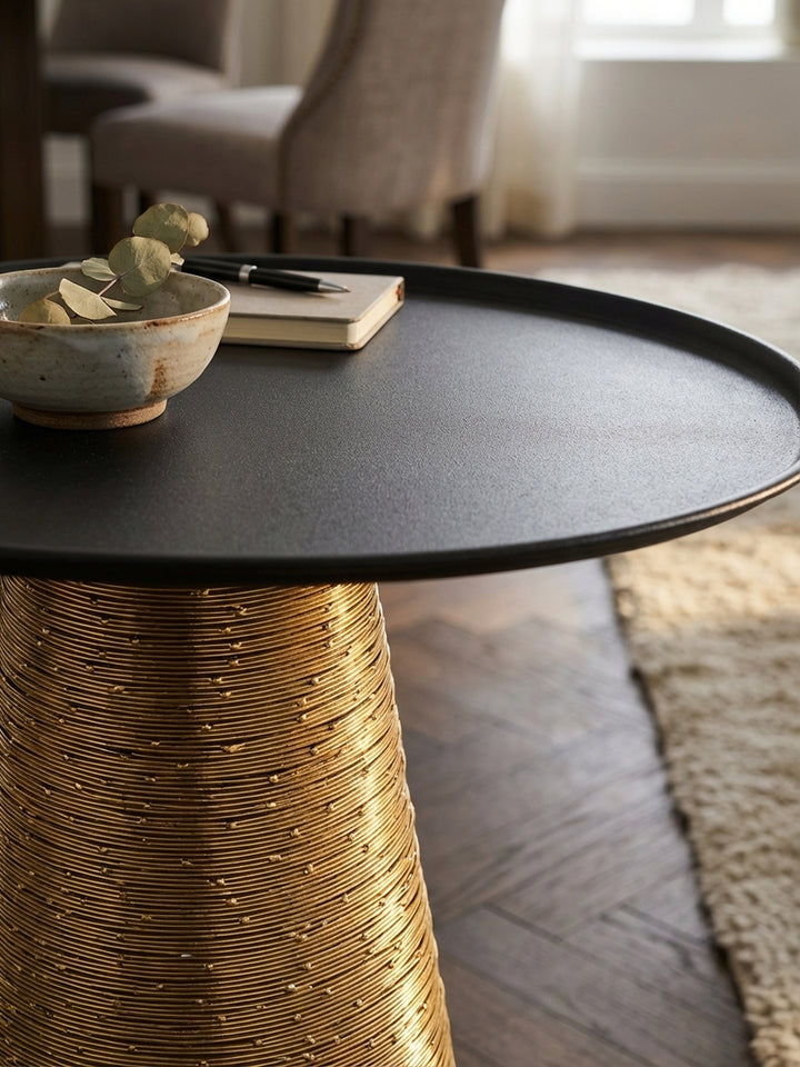 Detailaufnahme des goldfarbenen Standfußes aus Aluminium mit filigraner Drahtwicklung, die die hochwertige und strukturierte Oberfläche des modernen Sofatisches detailliert zeigt._
