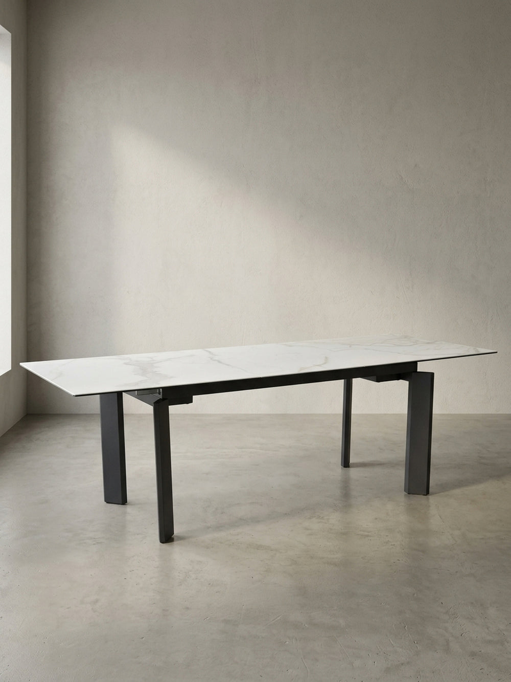 Frontansicht des bis 240 cm ausziehbaren Esszimmertisches mit weißer Keramikglasplatte und schwarzen, geometrischen Metallbeinen._