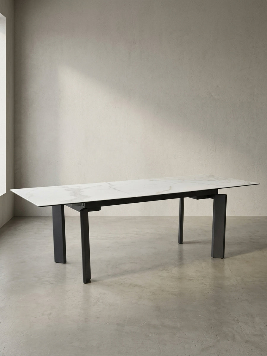 Frontansicht des bis 240 cm ausziehbaren Esszimmertisches mit weißer Keramikglasplatte und schwarzen, geometrischen Metallbeinen._