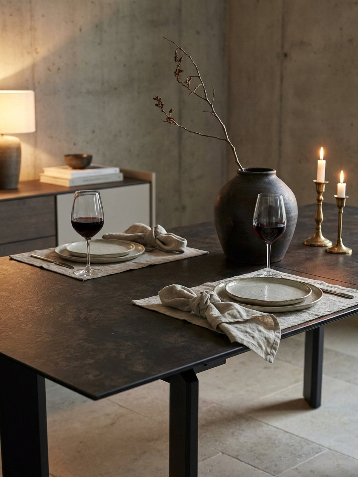 Nahaufnahme einer schwarzen Vase mit einer Pflanze auf einem Keramik-Esstisch, der für ein gemütliches Abendessen in einem stilvollen Esszimmer gedeckt ist._