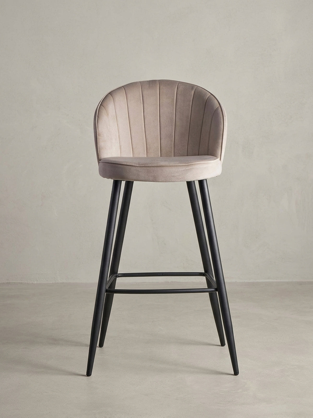 Skandinavischer Barhocker aus Samt in Beige, 3/4-Ansicht, die die geschwungene Rückenlehne und die stabile Konstruktion des Hockers betont.