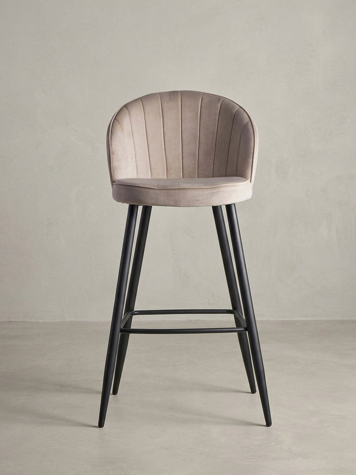 Skandinavischer Barhocker aus Samt in Beige, 3/4-Ansicht, die die geschwungene Rückenlehne und die stabile Konstruktion des Hockers betont._