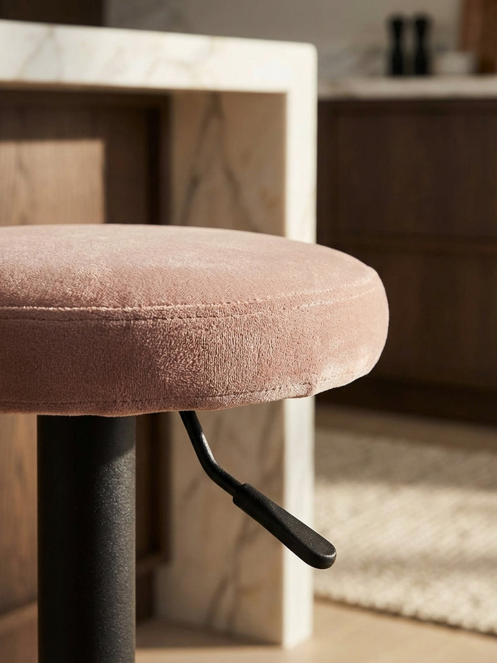 Detailaufnahme der weichen Samtstruktur des rosa Barhockers, die hochwertige Haptik und die feine Verarbeitung des Stoffes betonend._