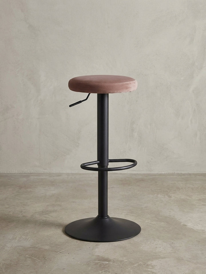 Moderner Barhocker in Rosa aus der 3/4-Ansicht, der die drehbare Funktion und den eleganten Kontrast von Samt und Metall zeigt._
