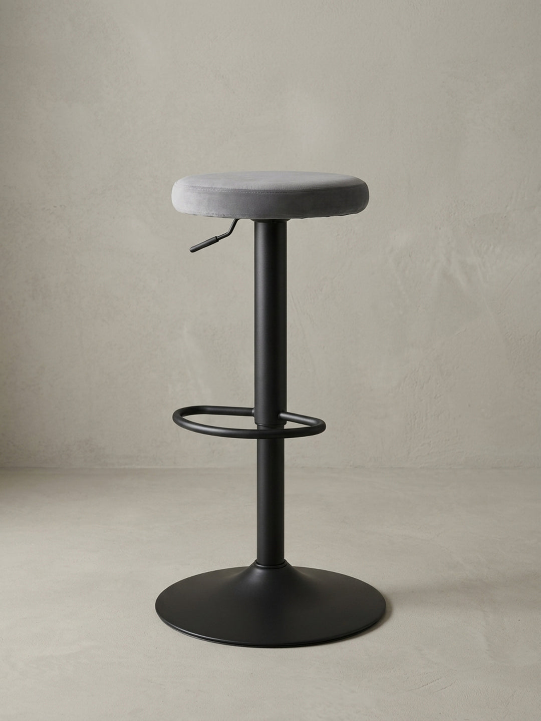 Drehbarer Design-Barhocker in Dunkelgrau aus Samt und Metall in einer 3/4-Ansicht, die die schlanke Silhouette und die Fußstütze hervorhebt._