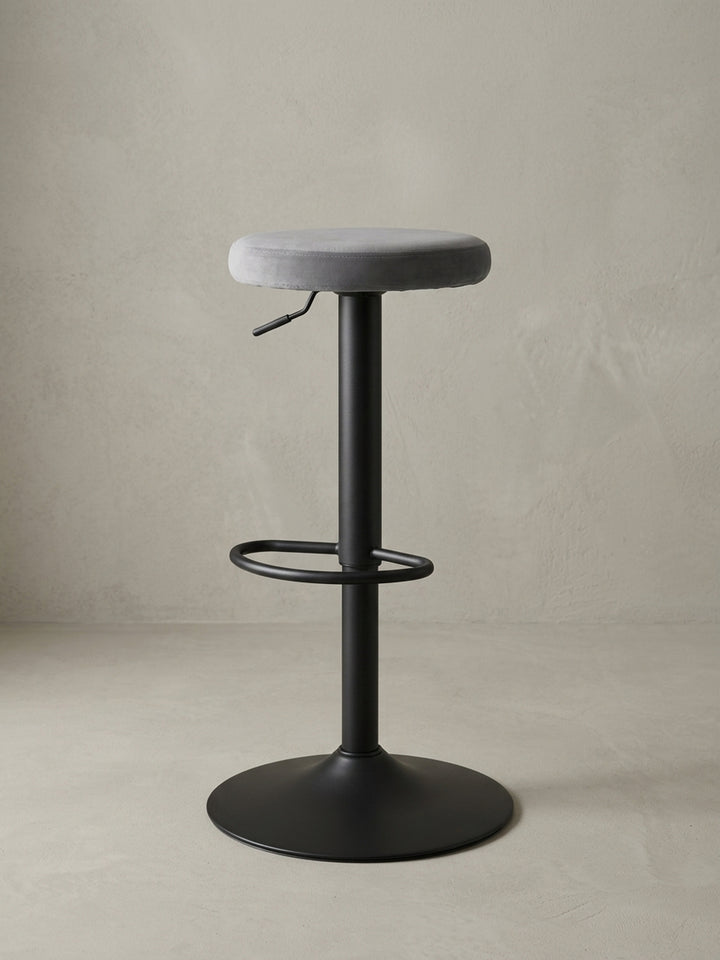 Drehbarer Design-Barhocker in Dunkelgrau aus Samt und Metall in einer 3/4-Ansicht, die die schlanke Silhouette und die Fußstütze hervorhebt._