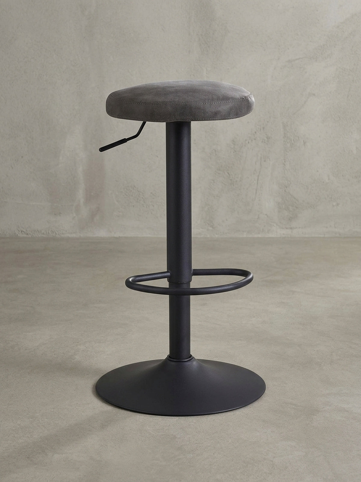 Design-Barhocker in 3/4-Ansicht, der die runde Sitzfläche aus grauem Stoff und den schlanken, höhenverstellbaren Standfuß aus mattschwarzem Metall hervorhebt._