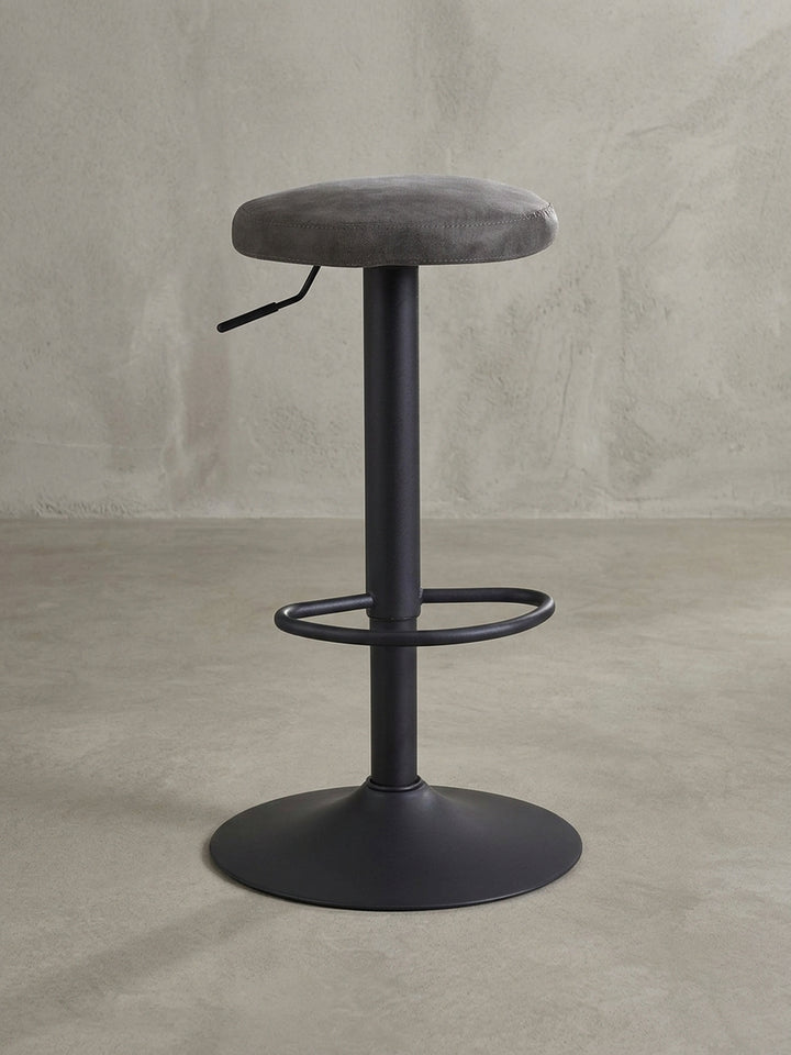 Design-Barhocker in 3/4-Ansicht, der die runde Sitzfläche aus grauem Stoff und den schlanken, höhenverstellbaren Standfuß aus mattschwarzem Metall hervorhebt._