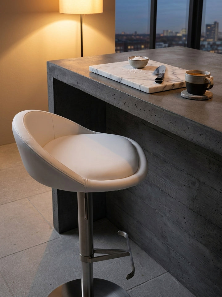 Weißer Design-Bistrohocker an der puristischen Hausbar neben einem mattschwarzen Tablett mit Kristallkaraffe und schweren Whiskeygläsern._