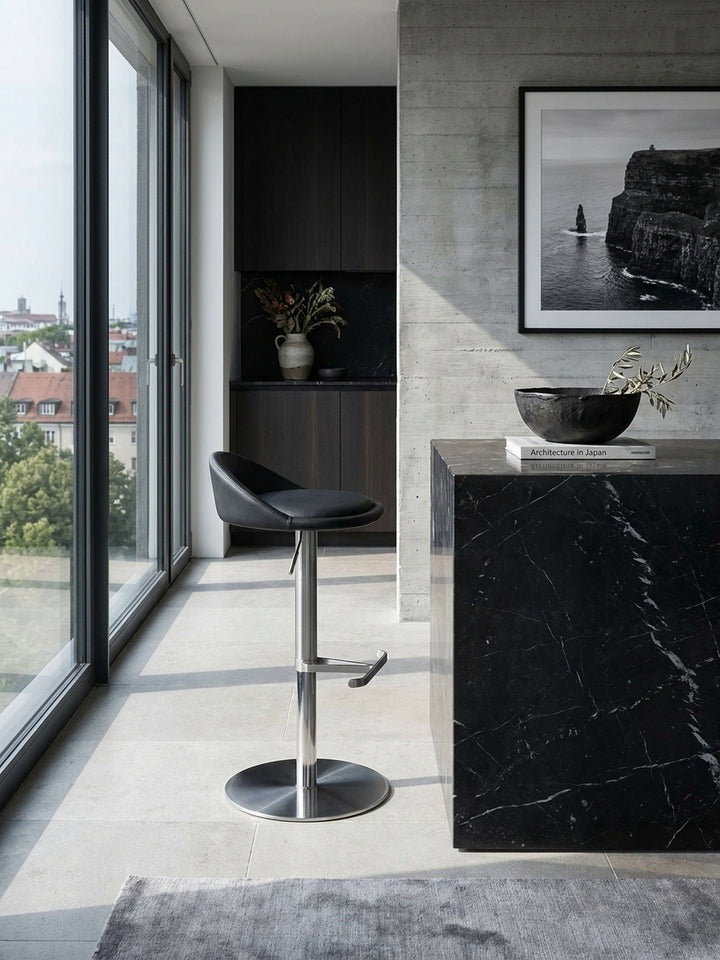 Zwei minimalistische Barstühle aus schwarzem Kunstleder und gebürstetem Edelstahl in perfekter Symmetrie am monolithischen Küchentresen._