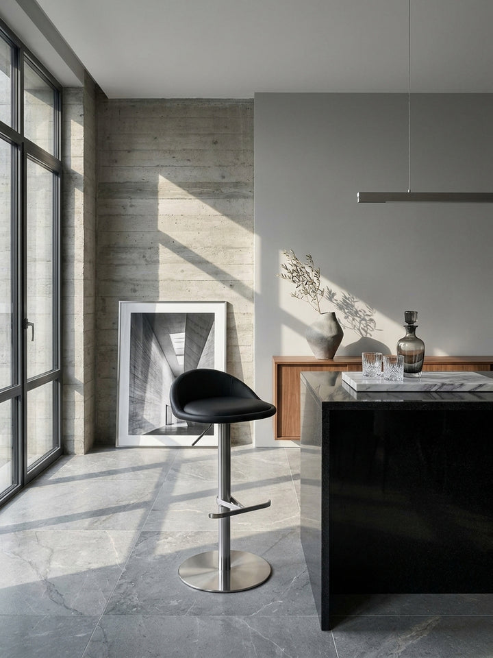 Eleganter Barhocker in Schwarz mit Edelstahlgestell an einer massiven Granit-Kücheninsel in einem puristischen und modernen Loft._