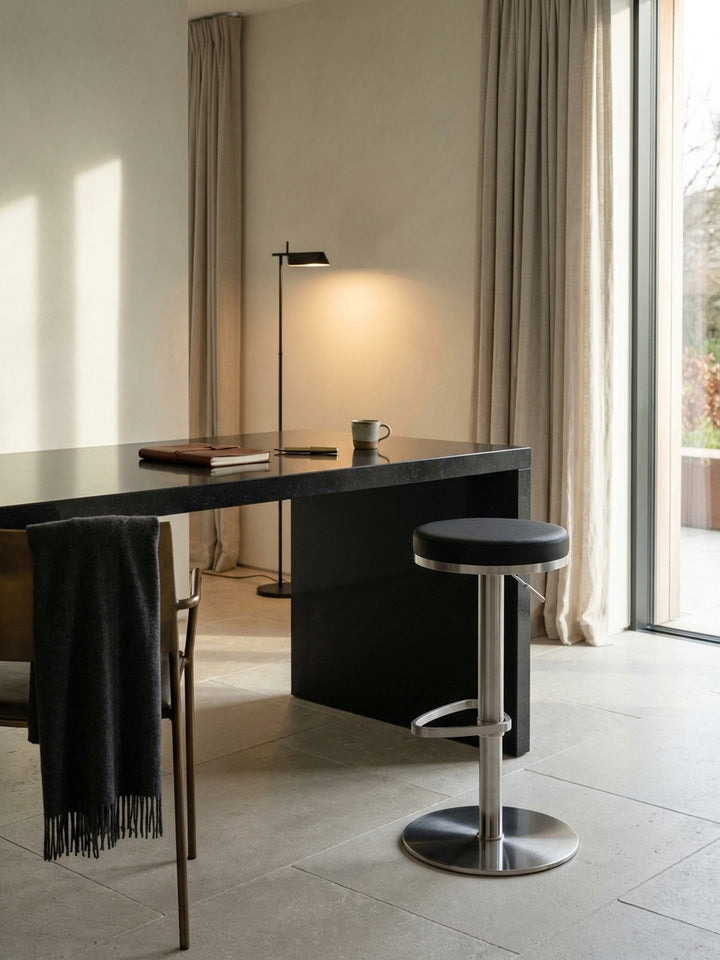 Zwei drehbare Bistrohocker in Schwarz und Silber nebeneinander an einem hohen Küchentresen unter einer linearen Pendelleuchte._