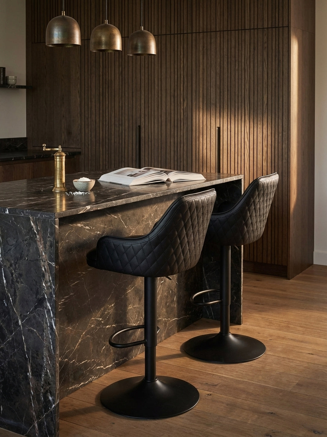 Ein Glas Wein auf der Kücheninsel aus Marmor neben dem schwarzen Leder-Barhocker, das eine entspannte Feierabendstimmung erzeugt._