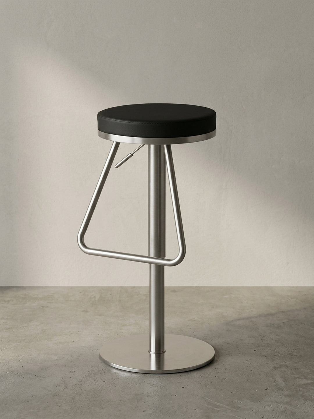 Dreiviertelansicht des modernen Thekenhockers, welche die elegante dreieckige Fußablage und den stufenlos höhenverstellbaren Metallzylinder betont._
