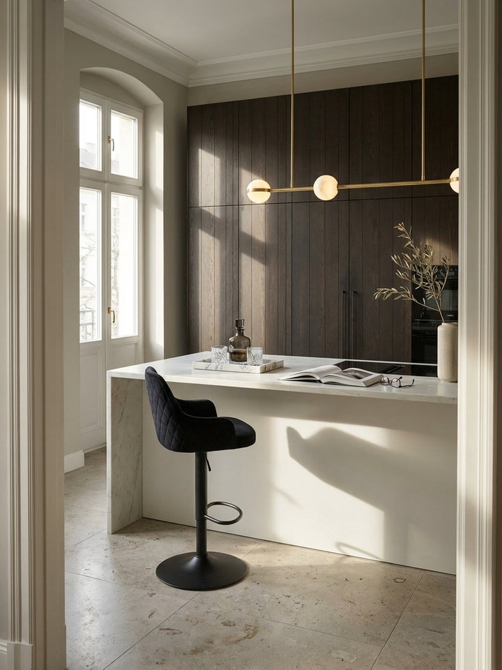 Eleganter schwarzer Samt-Barhocker mit Rautensteppung an einer hellen Quarzit-Kochinsel in einer luxuriösen Altbauküche mit Kalksteinboden und Messing-Akzenten._