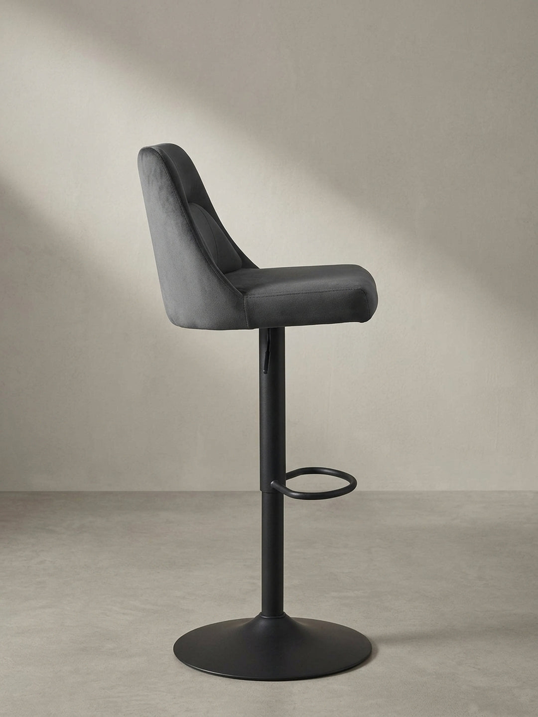 Design-Barstuhl aus grauem Samt in der Dreiviertelansicht, die ergonomisch geformte Sitzschale und die Fußstütze zeigend._