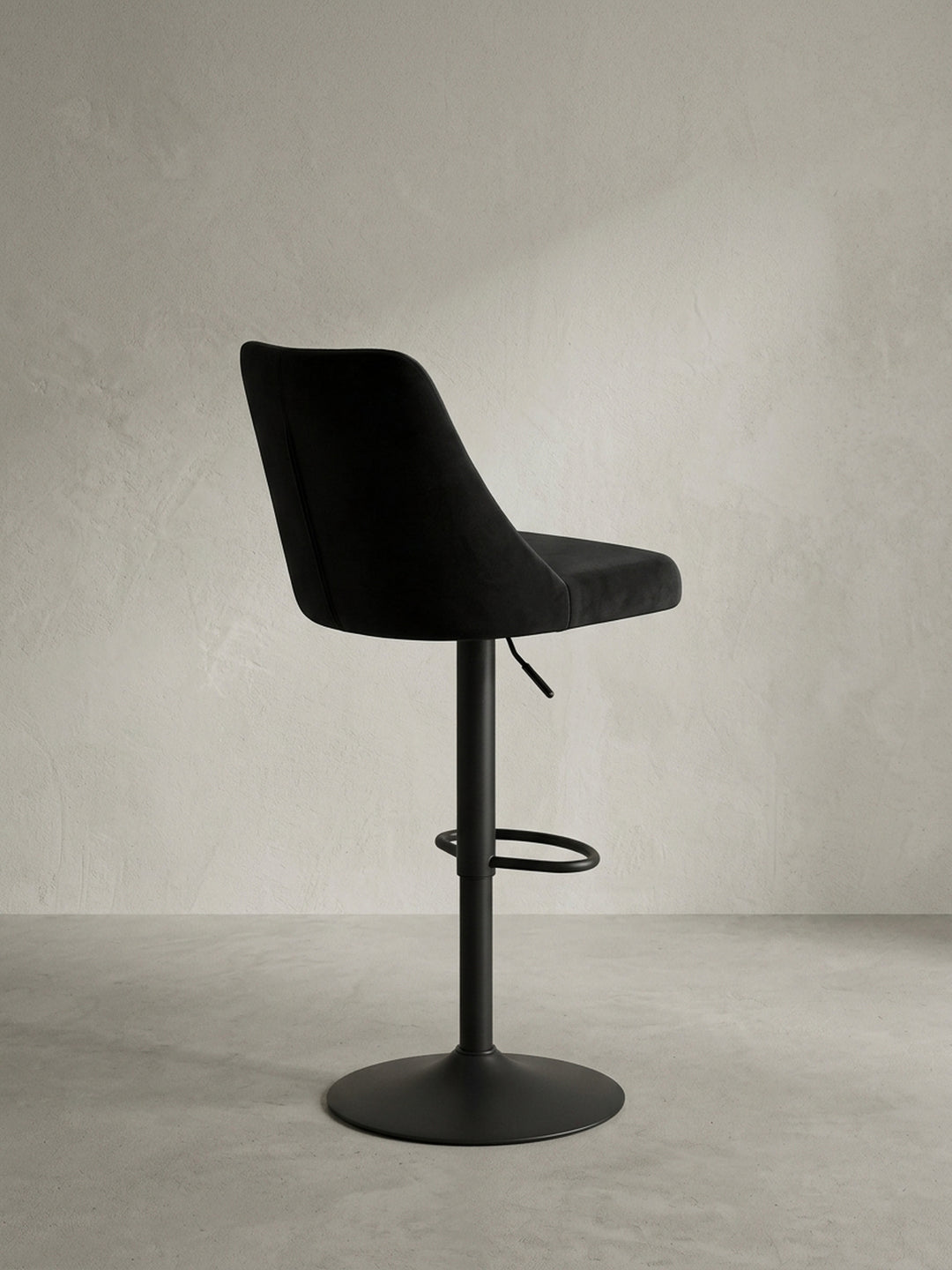 Detailaufnahme des Hebels zur Höhenverstellung und des Übergangs vom Samtsitz zum mattschwarzen Metallfuß des Design-Barstuhls._