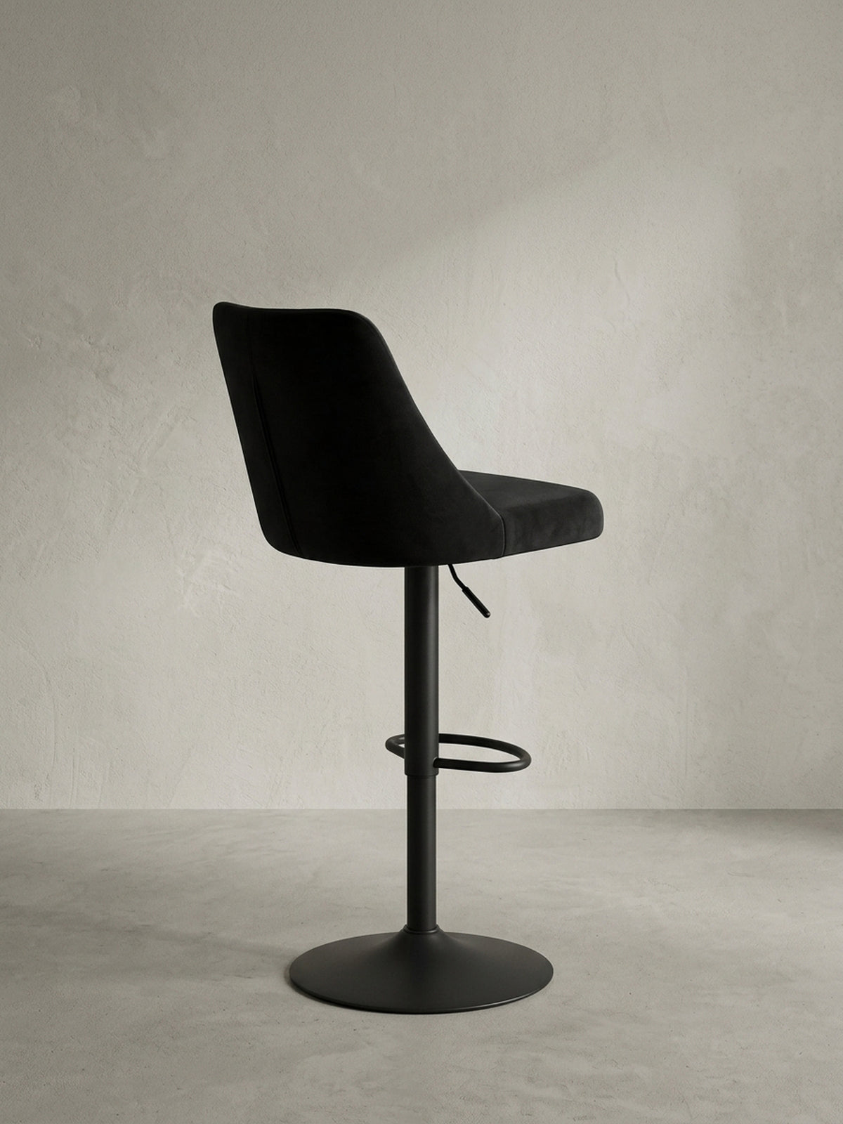 Detailaufnahme des Hebels zur Höhenverstellung und des Übergangs vom Samtsitz zum mattschwarzen Metallfuß des Design-Barstuhls._