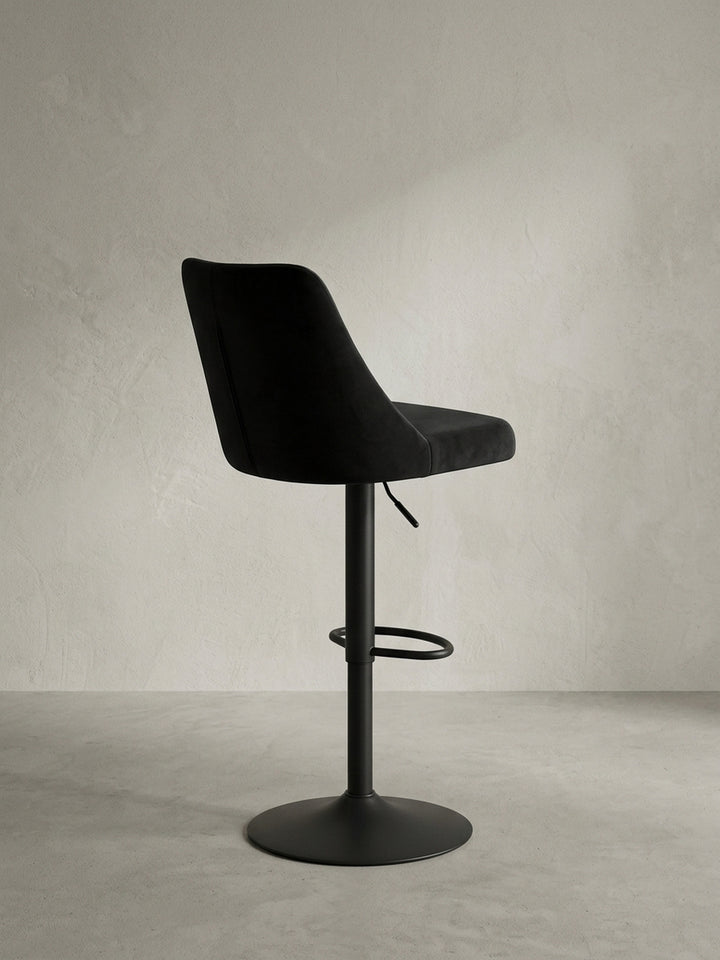 Detailaufnahme des Hebels zur Höhenverstellung und des Übergangs vom Samtsitz zum mattschwarzen Metallfuß des Design-Barstuhls._