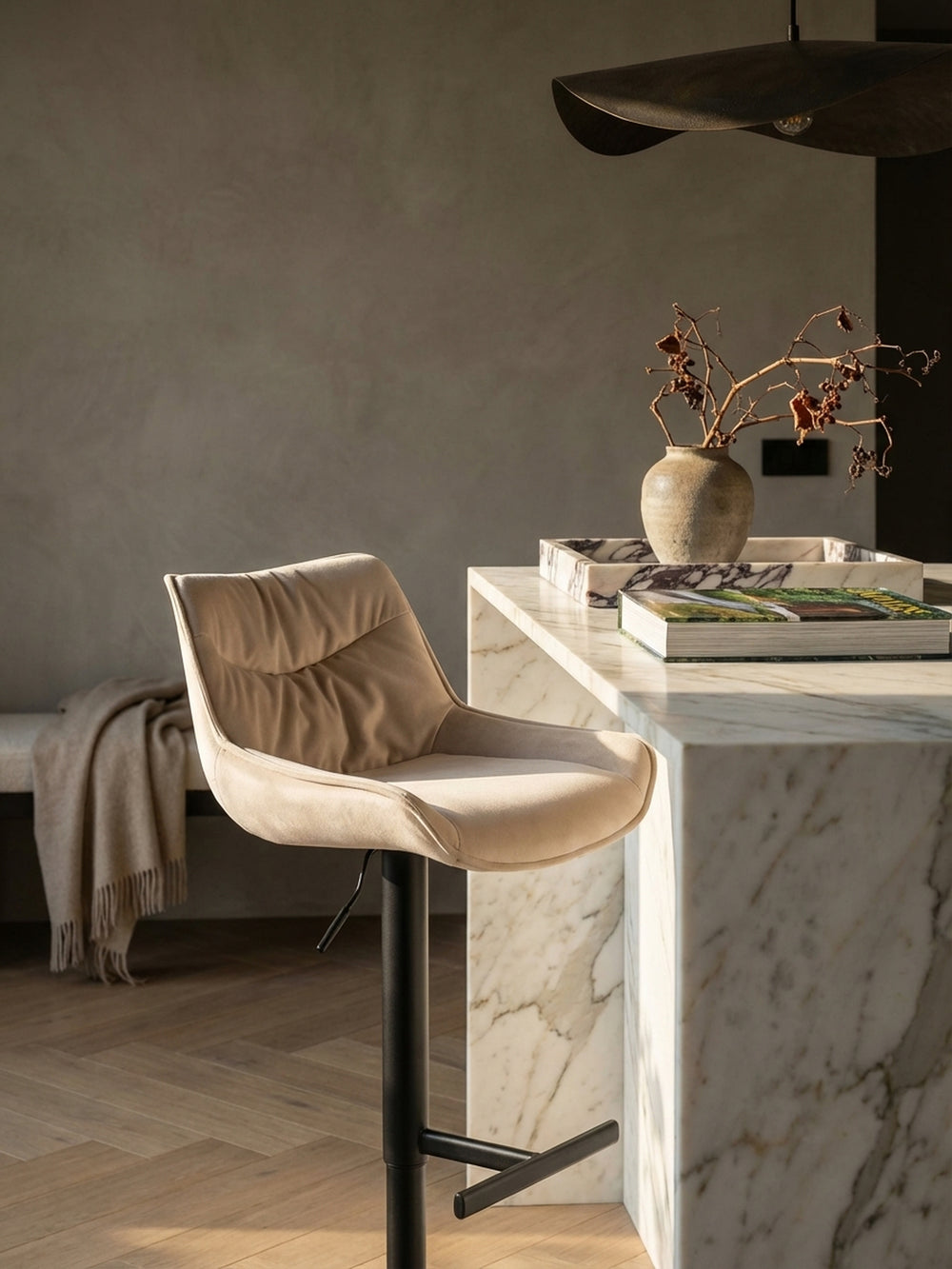 Ein gemütlicher Morgen an der Küchentheke mit dem beigen Samt-Barhocker, neben einer Tasse Kaffee und einem Architekturmagazin auf der Marmorplatte._