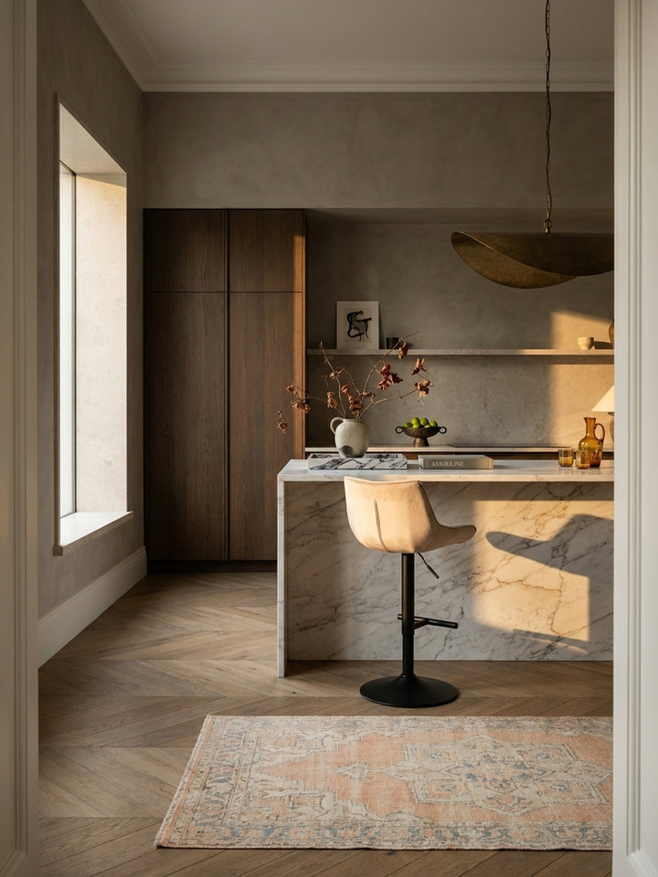 Eleganter Barhocker aus beigem Samt an einer minimalistischen Kücheninsel aus Marmor in einem lichtdurchfluteten Penthouse mit Eichenparkett._