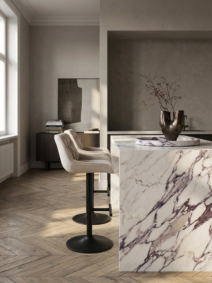 Der designstarke Barhocker aus beigem Samt als perfekte Ergänzung zu dunklen Eichenholz-Küchenschränken und einer Arbeitsplatte aus Naturstein._