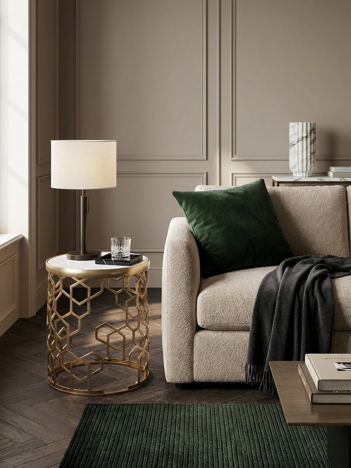 Draufsicht auf den runden Marmor-Beistelltisch neben einer Couch, der das goldene geometrische Metallgestell und die Tischdeko aus Tasse und Figur zeigt.