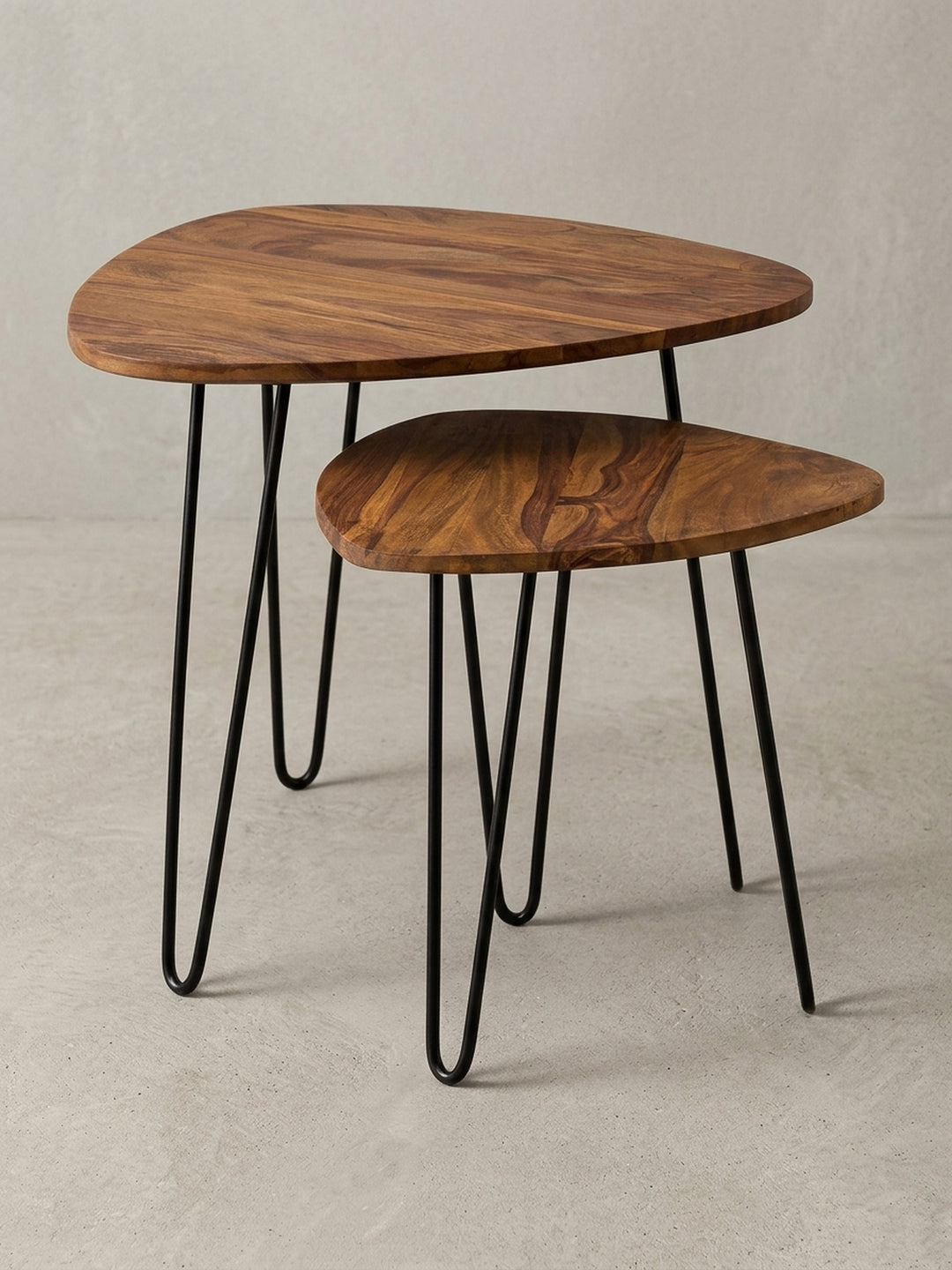 Zweiteiliger Holz Satztisch mit dreieckig abgerundeten Platten und schwarzen Metallbeinen. Der Couchtisch kombiniert warmes Sheeshamholz mit minimalistischem Industrial Design._