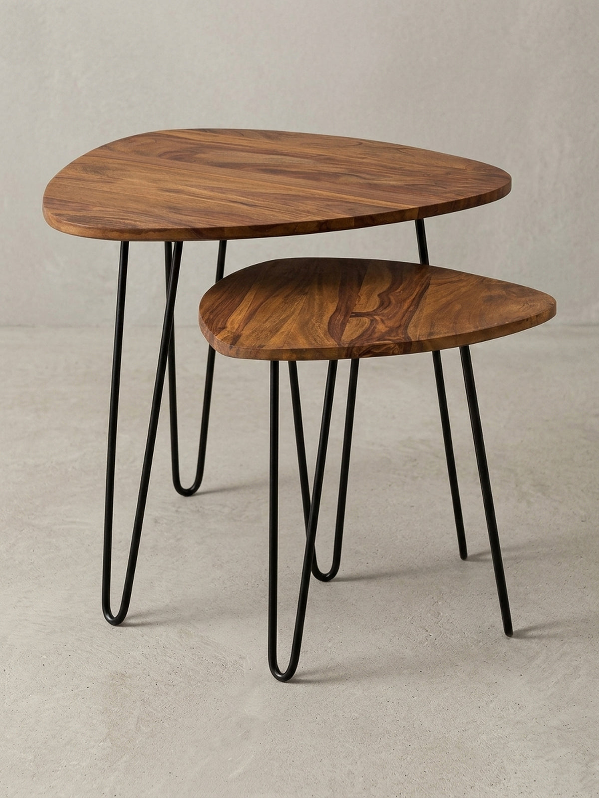 Zweiteiliger Holz Satztisch mit dreieckig abgerundeten Platten und schwarzen Metallbeinen. Der Couchtisch kombiniert warmes Sheeshamholz mit minimalistischem Industrial Design._