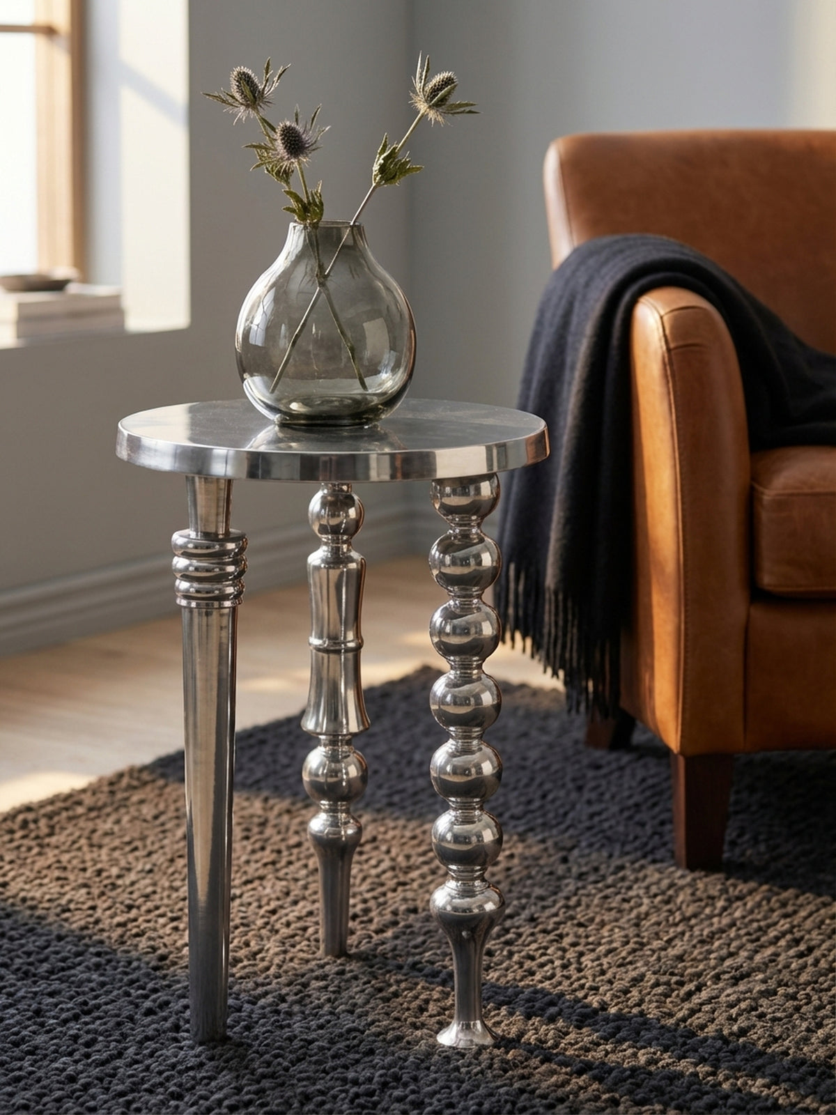 Design-Vignette mit dem silbernen Dekotisch, auf dem eine einzelne Vase mit einer getrockneten Blume steht und so einen minimalistischen Akzent setzt._