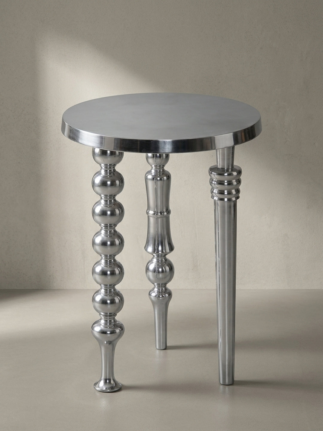 Frontansicht des modernen Beistelltisches aus silbernem Aluminium mit seinen drei kunstvoll gestalteten, unterschiedlichen Beinen auf weißem Hintergrund._