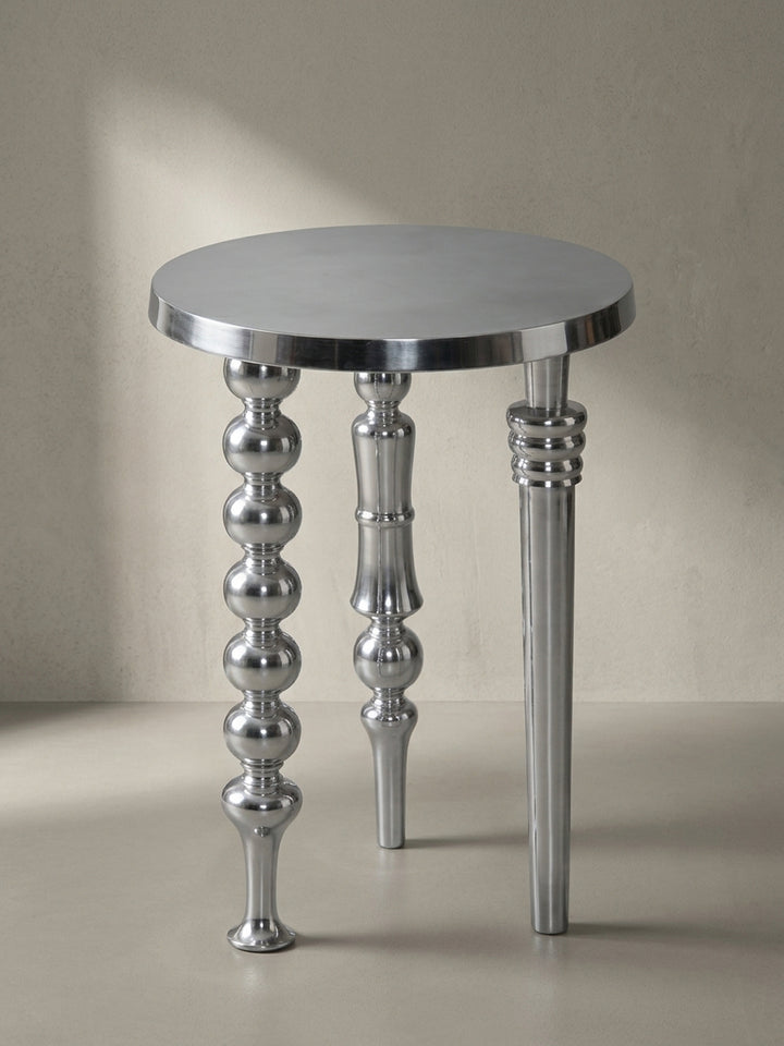 Frontansicht des modernen Beistelltisches aus silbernem Aluminium mit seinen drei kunstvoll gestalteten, unterschiedlichen Beinen auf weißem Hintergrund._